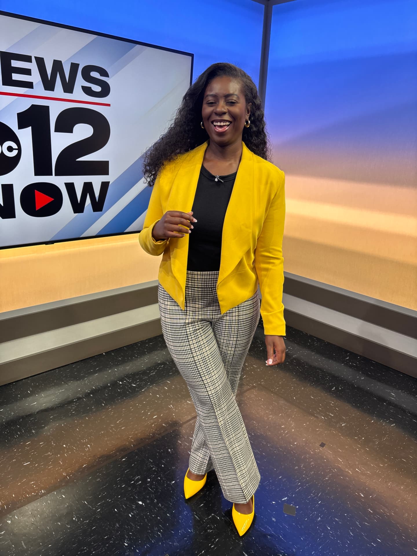 Moriah Davis laughing on a television news set in a yellow blazer